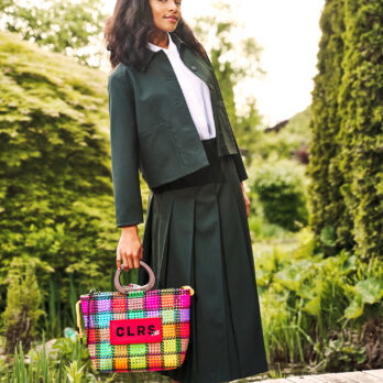 Stylish woman in green suit holding a vibrant, handwoven CLRS by SAAT tote outdoors.