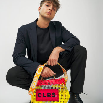 Male model in a black suit holding a handwoven CLRS by SAAT tote bag in pink and yellow.
