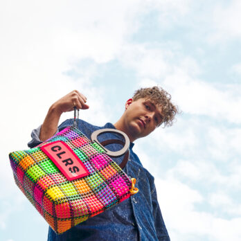 Smiling man holding a pink and green CLRS by SAAT tote in front of a bright sky.